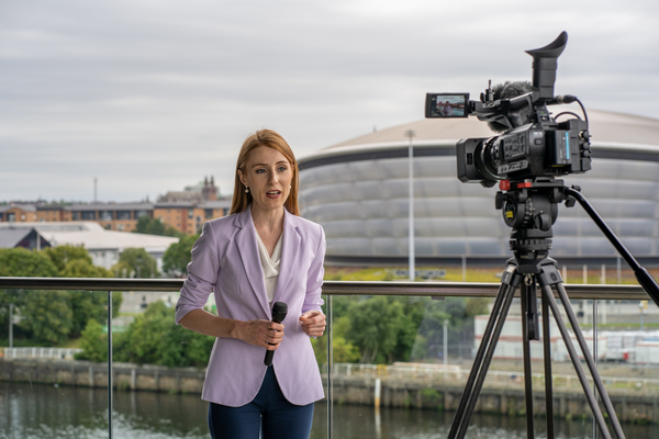 An image of our postgraduate alumni, Vanessa, standing in front of a camera for the complete your application guide link. 