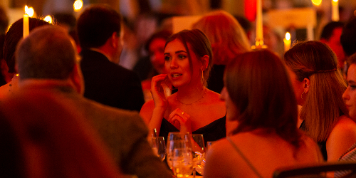 People at a gala dinner, sitting around candlelit tables and talking