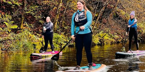 Three Occupational Therapy students paddle boarding on a river.