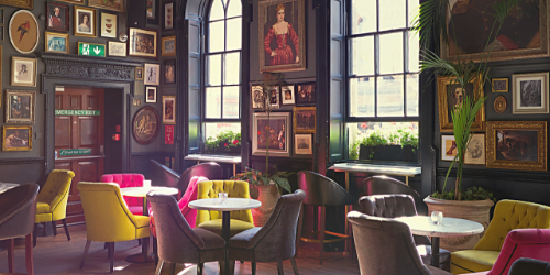 The interior of an empty restaurant. There are tables and chairs, and many paintings on the walls. 