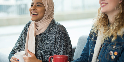 Two girls sitting with a cup of tea, laughing 