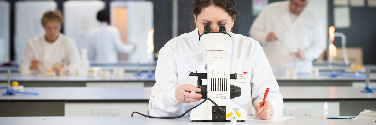 Edinburgh Napier student testing samples under a microscope in our microbiology lab at Sighthill. 
