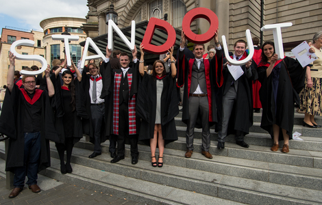 Students after the graduation ceremony at usher hall holding up letters that spell out 'stand out' with the word 'do' in a different colour