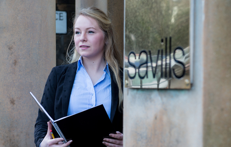 Student beside savilles sign holding a book open in her hands