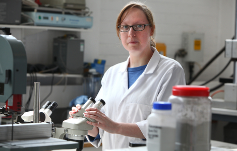Student with her hands on a microscope as she looks at the camera