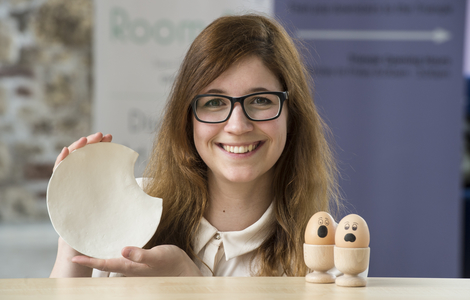 Martina Zupan smiling and holding up her eggshell tableware to the camera
