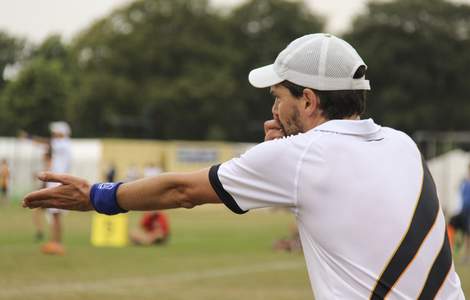 Back of a man wearing sporty clothes with his hand outstretched and blowing on a whilste