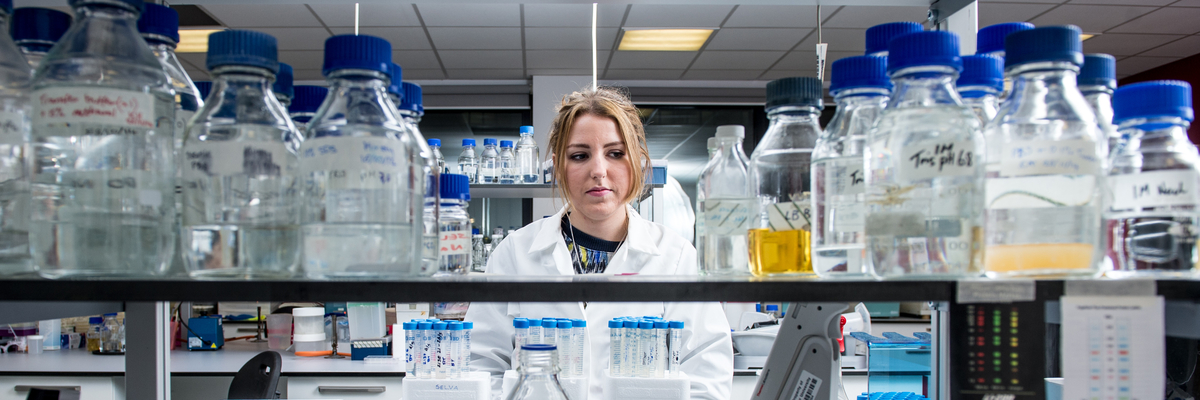 Scientist standing behind shelves of laboratory equipment