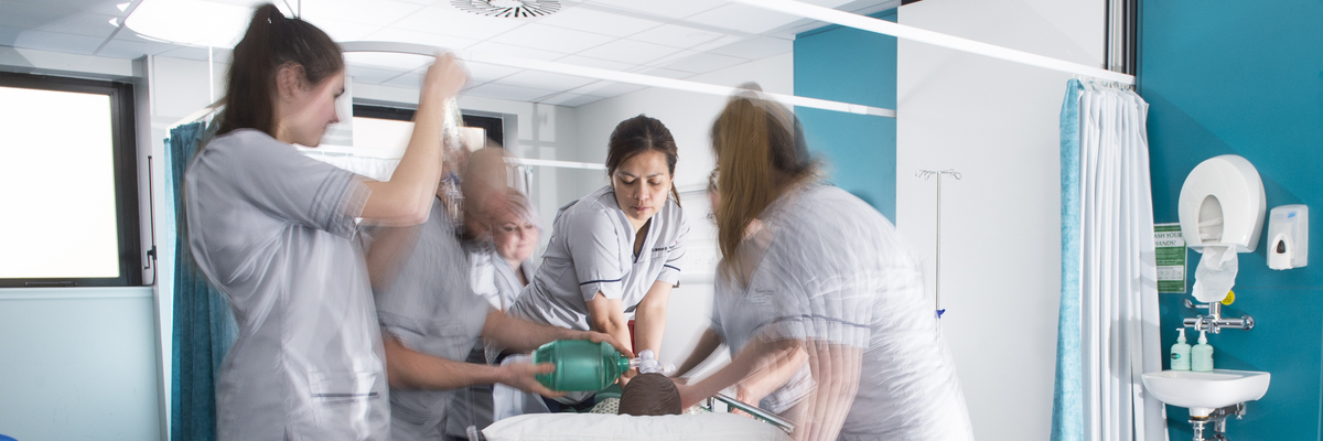 Nursing students grouped around a 'patient' mannequin