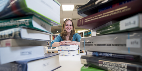 Woman smiling behind stacks of books