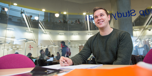 Photo of a student at Edinburgh Napier University looking up and smiling as he works with a pen in his hand