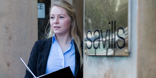 Student standing beside a Savills sign outside their offices