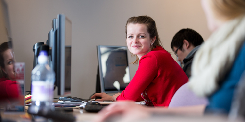 Students using computers to study with one student looking at the camera and smiling