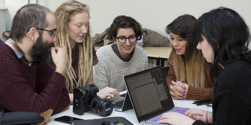 Photography students grouped around a laptop, working on a project