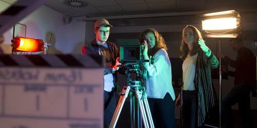 Three students filming with a directors clapboard held in front