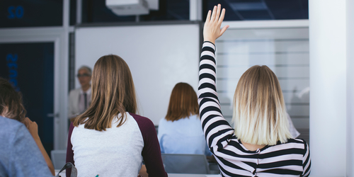 Image taken from behind Students with their hand up to ask a question during a lecture