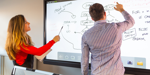 User Experience students standing beside an interactive whiteboard sketching a wireframe for a project