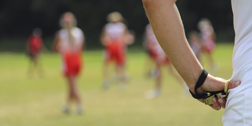 Person Sport officiating with their hands on their hips, players on the pitch are out of focus