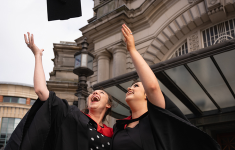 Two graduating women throwing their graduation caps in the air outside Usher Hall, wearing graduation gowns and looking very happy.