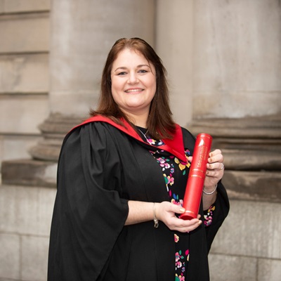 Claire Yilmaz on graduation day, dressed in graduation gown and holding parchment 