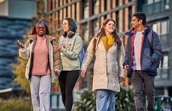 Four students from Edinburgh Napier University walking and conversing in the sunlight within the warm backdrop of Edinburgh Napier student accommodation.
