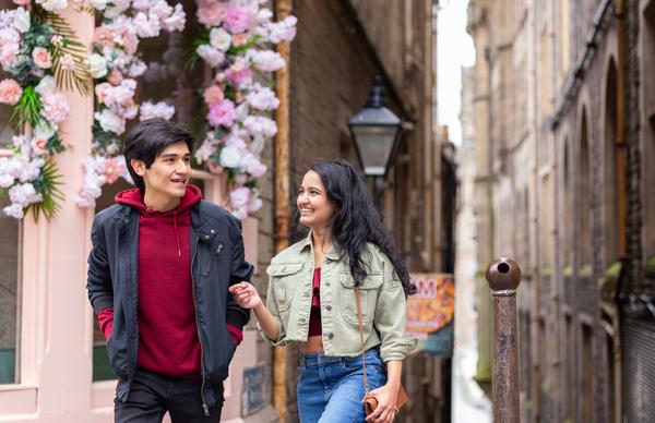 Two students from Edinburgh Napier University strolling around the iconic old town of Edinburgh's city centre on a sunny day, smiling and chatting. 
