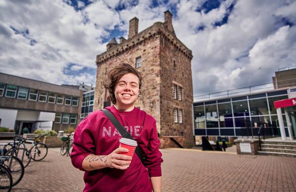 Undergraduate student looking at the camera and smiling in front of the old Merchiston tower, where John Napier lived.  