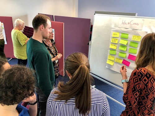 A group of staff attending a strategy engagement session, looking at some collected post-it notes on a board