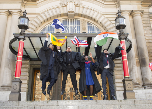Group of International MBA graduates in their graduation attire, throwing flags and jumping, after their graduation ceremony, outside Usher Hall. 