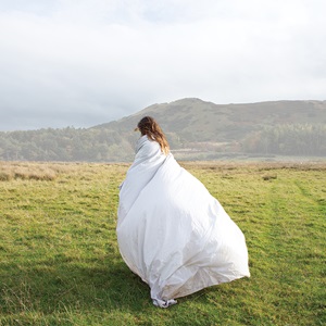 A model poses in grassy field wrapped in white bedding