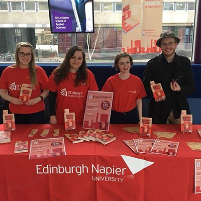 Student ambassadors standing behind a table display for the Edinburgh Napier Big Read