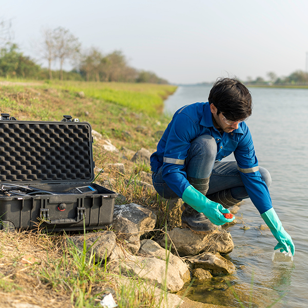 A student wearing gloves and doing water sampling by the side of a river