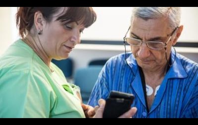 Healthcare practitioner watching an elder patient using a mobile phone