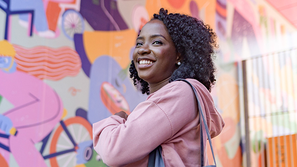 A smiling student stood outside a public artwork at Bainfield Student accommodation