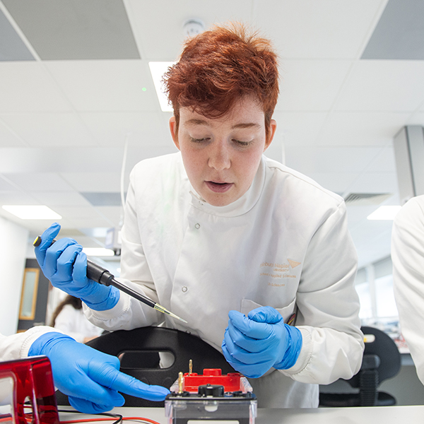 A science student in lab coat and blue gloves looks down, carefully pipetting