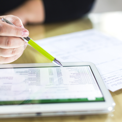 hand holding pen reading over spreadsheet on ipad