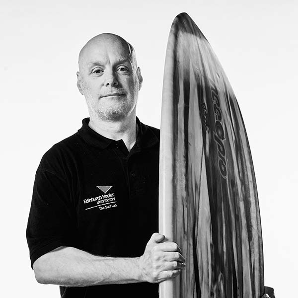 doctor brendon ferrier, professor and co-founder of the surf lab, stands confidently with his surf board.