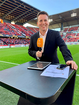 David Tanner stood holding a microphone in sports stadium