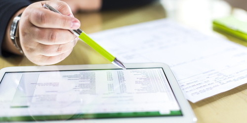 a close-up of a hand holding a pen pointing at an iPad with data on it