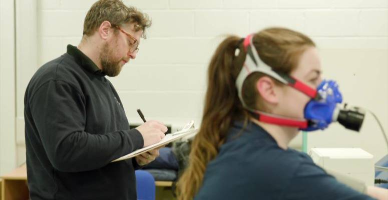 woman with ventilator mask, man in background taking notes